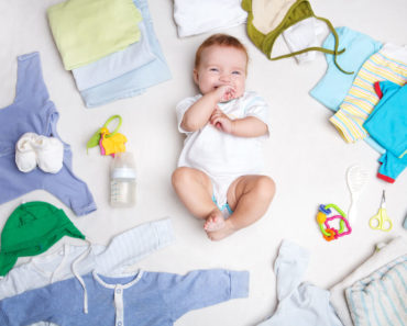 A baby surrounded with baby clothes.