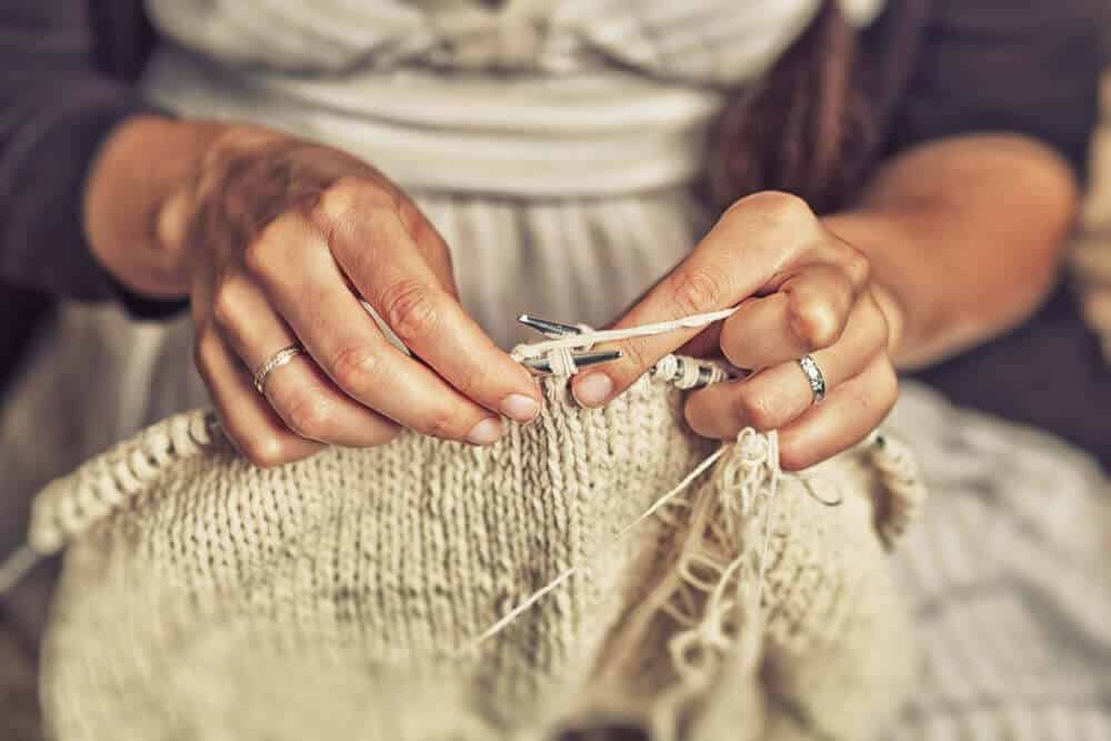 A closer shot of an old woman knitting an off-white yarn.