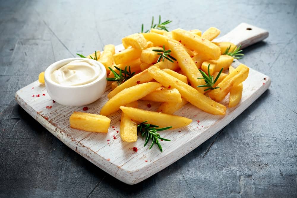 Baked fries served on a white wooden board.