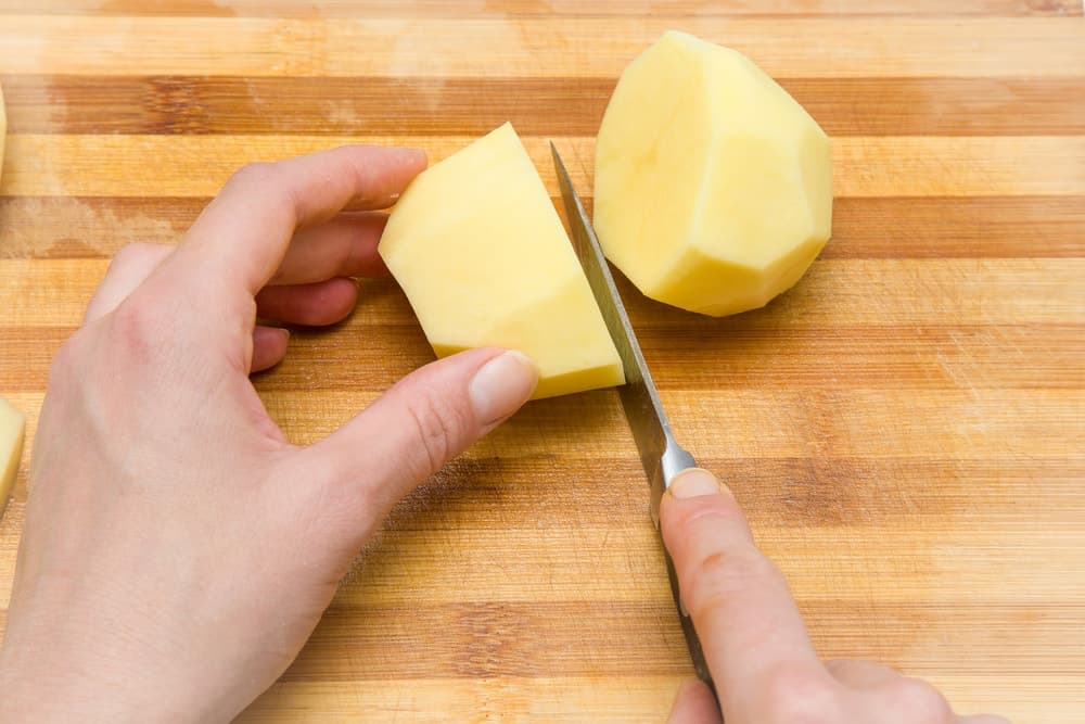 A potato is being cut in half to make french fries.