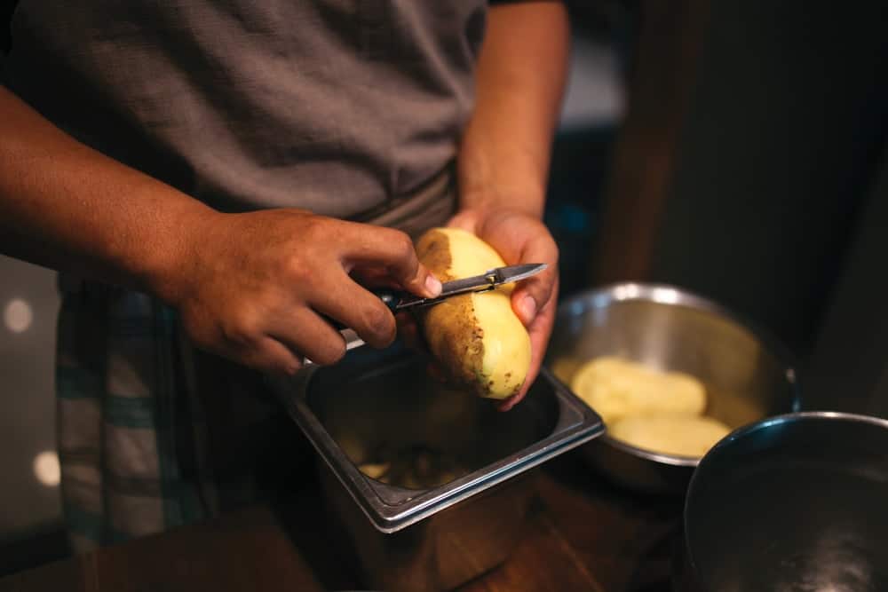 A cook is peeling potatoes to turn them into french fries.
