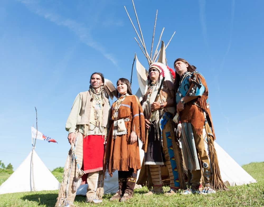 Members of the Native American tribe stand inf front of a wigwam.