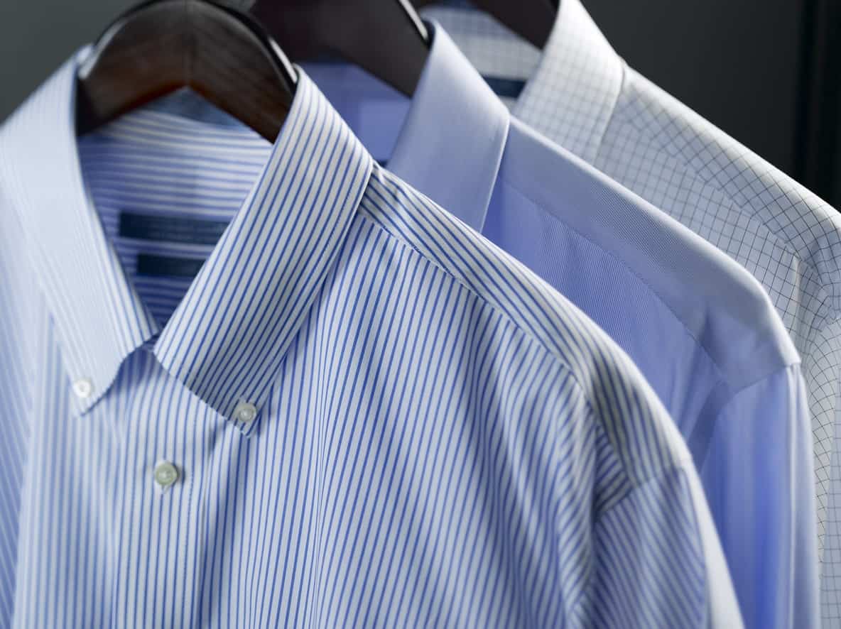 Three long sleeve shirts with button down collar on wooden clothes hanger.