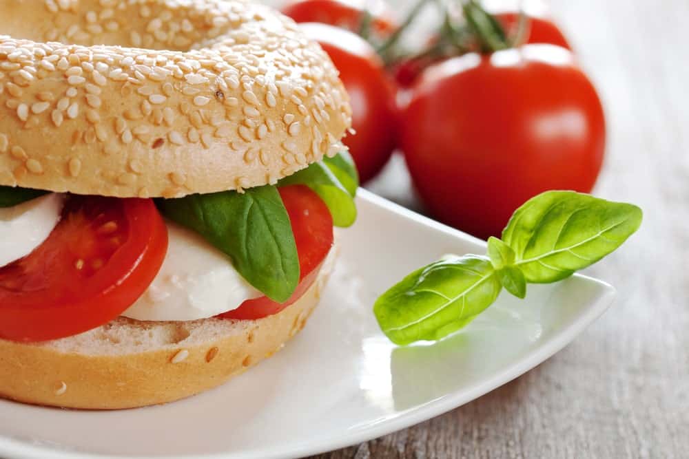 A plate of bagel sandwich with tomato and cheese beside fresh tomatoes.