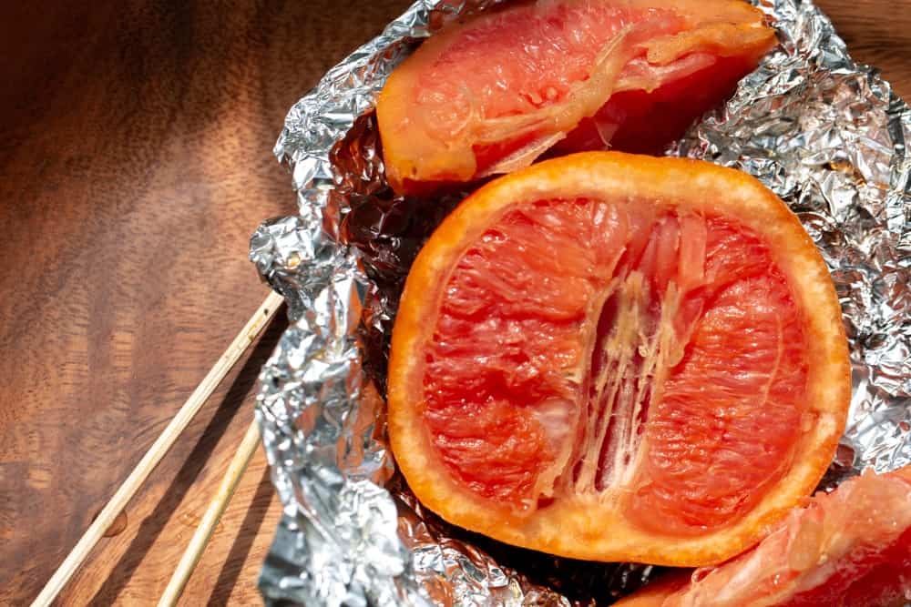 Slices of broiled grapefruit in a tin foil on wooden background.
