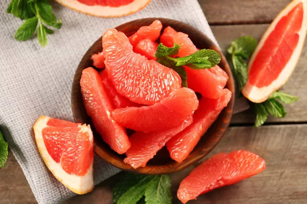 Slices of grapefruit on a wooden bowl and wooden background.