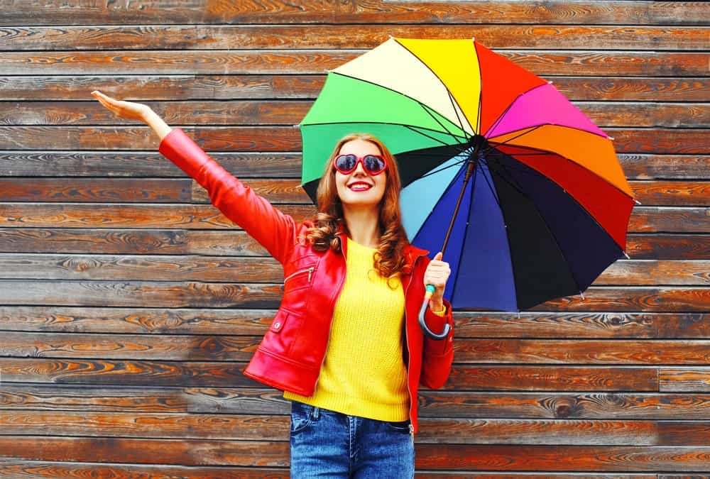 Woman in colorful outfit holding a rainbow-colored umbrella.