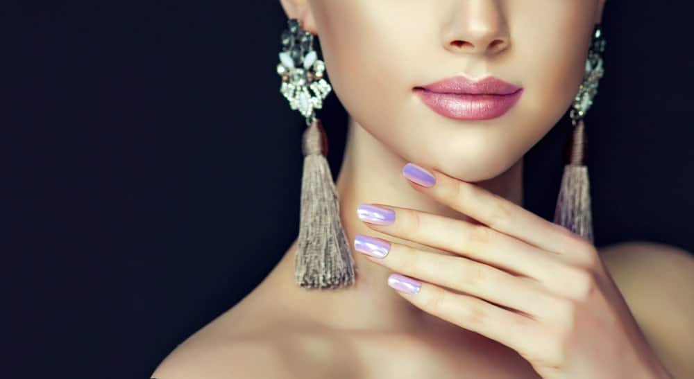 Woman with dangling earrings and colored nails wearing pearl lipstick.