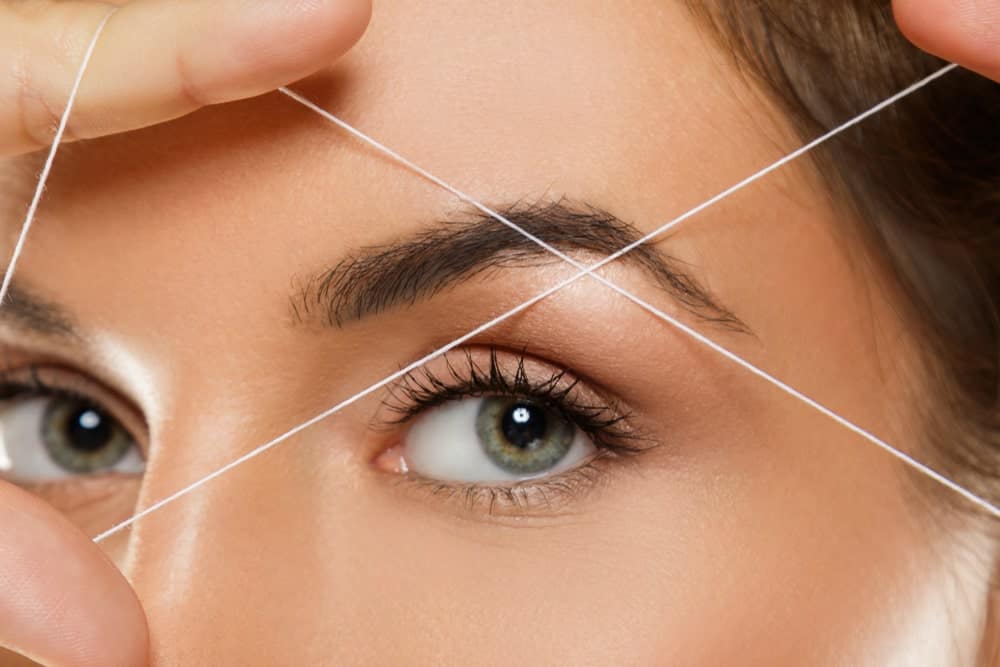 A woman holds a thread on her eyebrow for threading.