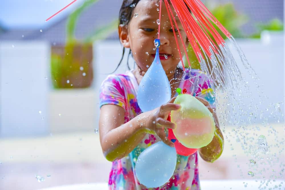 A young girl gets wet while playing with water balloons.