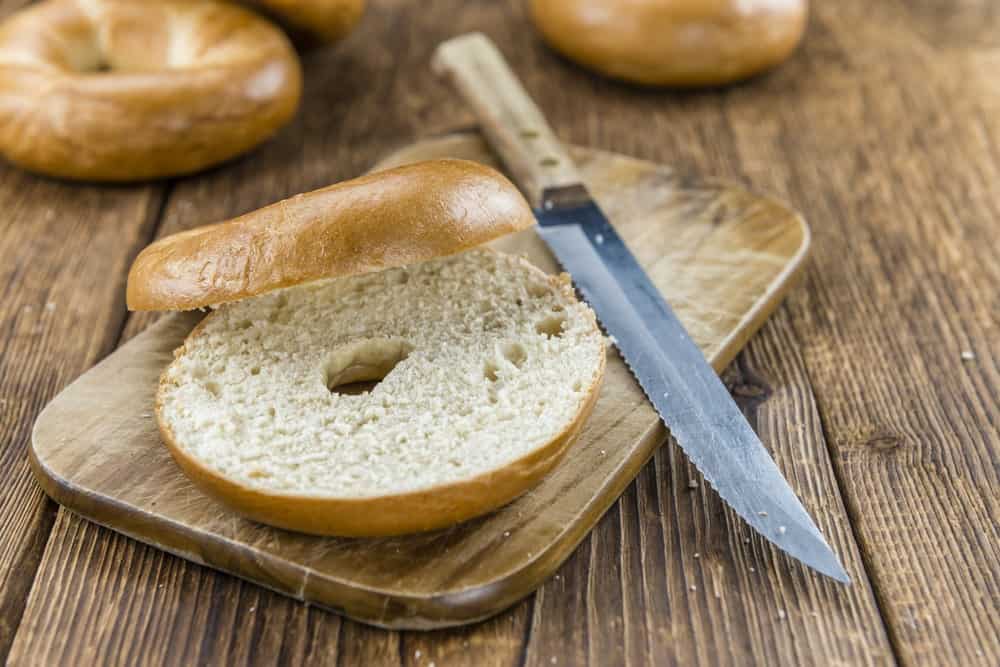 A half-cut bagel on a plate with a knife