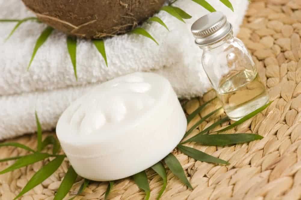 A small bottle of coconut oil beside a white container with leaves and white folded towels.