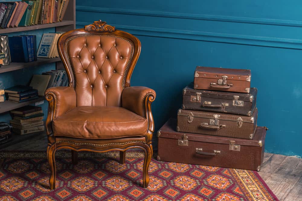 This is a close look at a brown leather tufted Bergere Chair beside a bookshelf.