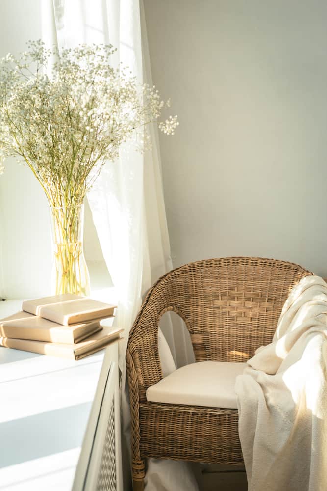 This is a close look at a reading nook by the window with a woven wicker tub chair that has a cushion.