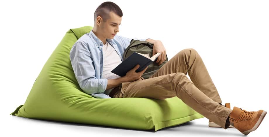 A man reading a book while sitting on a green bean bag chair.