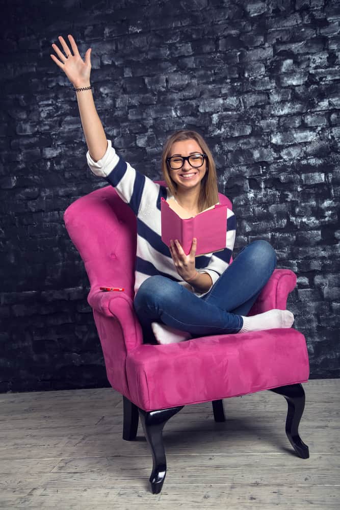 A woman reading a pink book on a pink club chair.