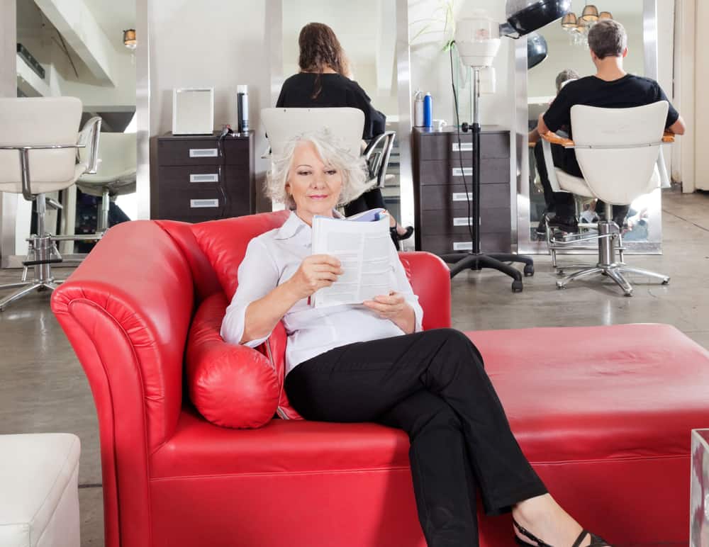 A woman reading a book on a red leather chaise lounge.