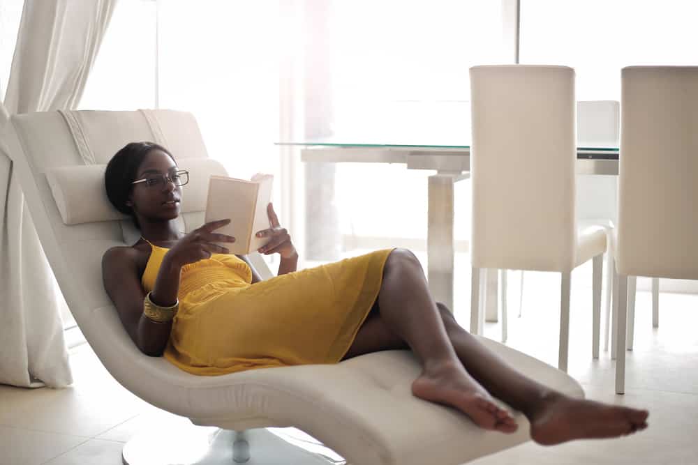 A woman reading a book on a white tufted recliner chair.