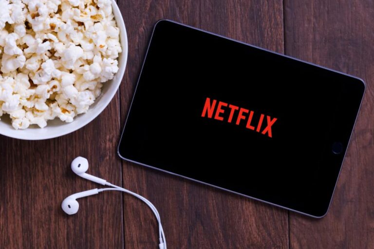 Ipad mini with Netflix logo alongside a bowl of popcorn and earphone.