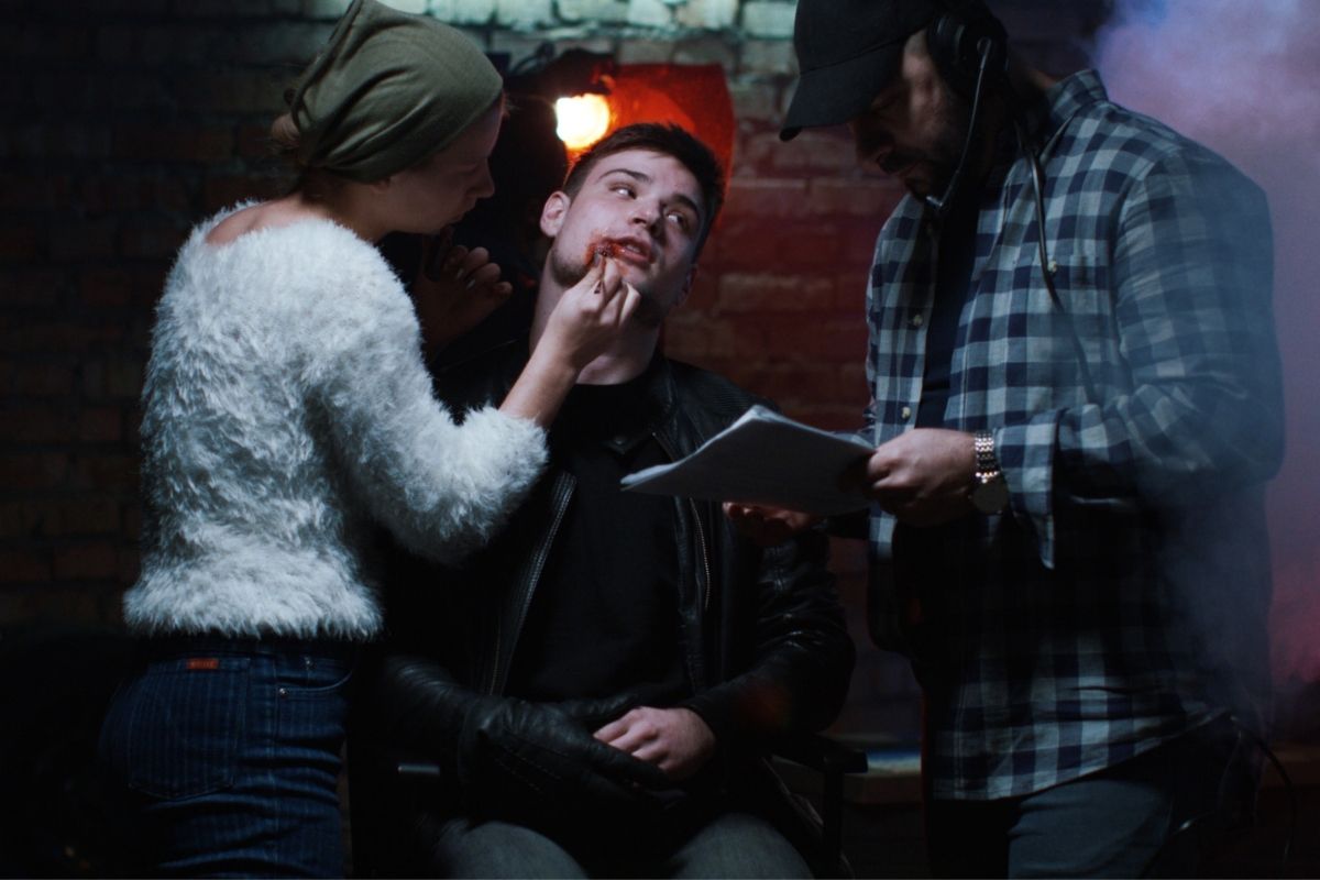 A photo of a makeup artist working with an actor on set.