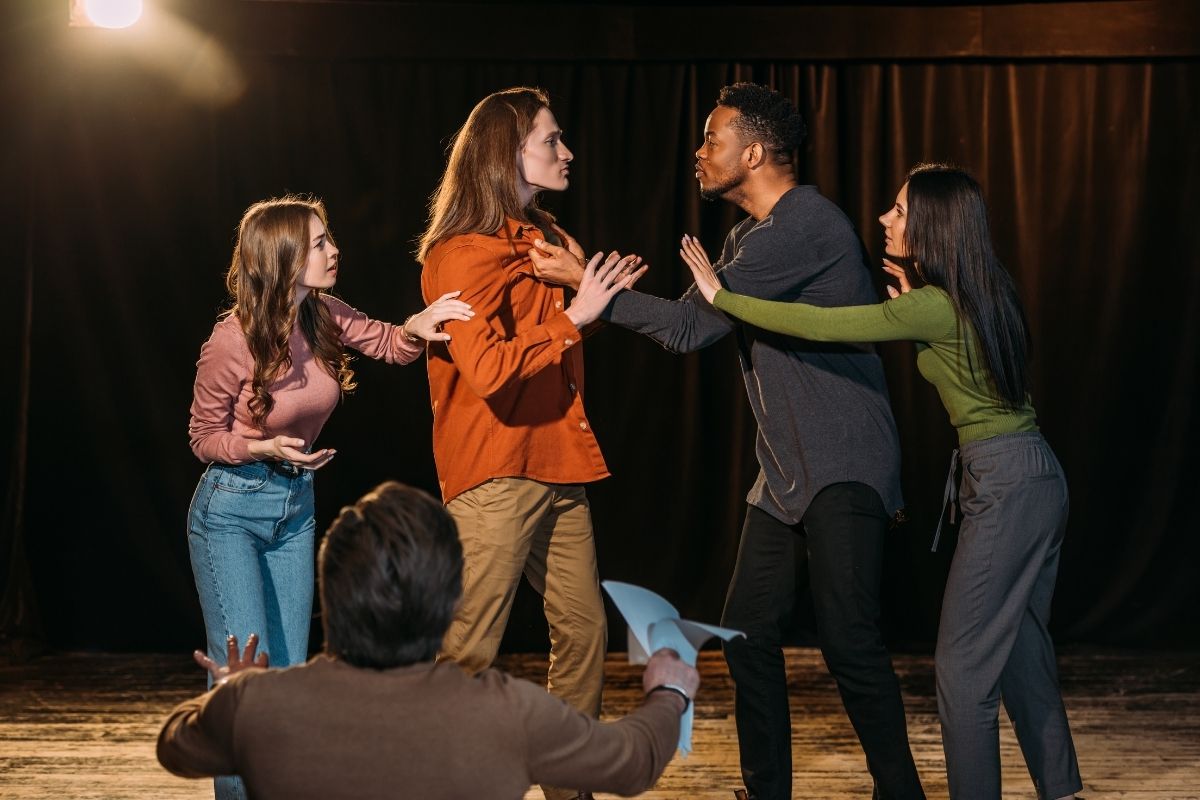 Actors and actresses rehearsing fight on stage.