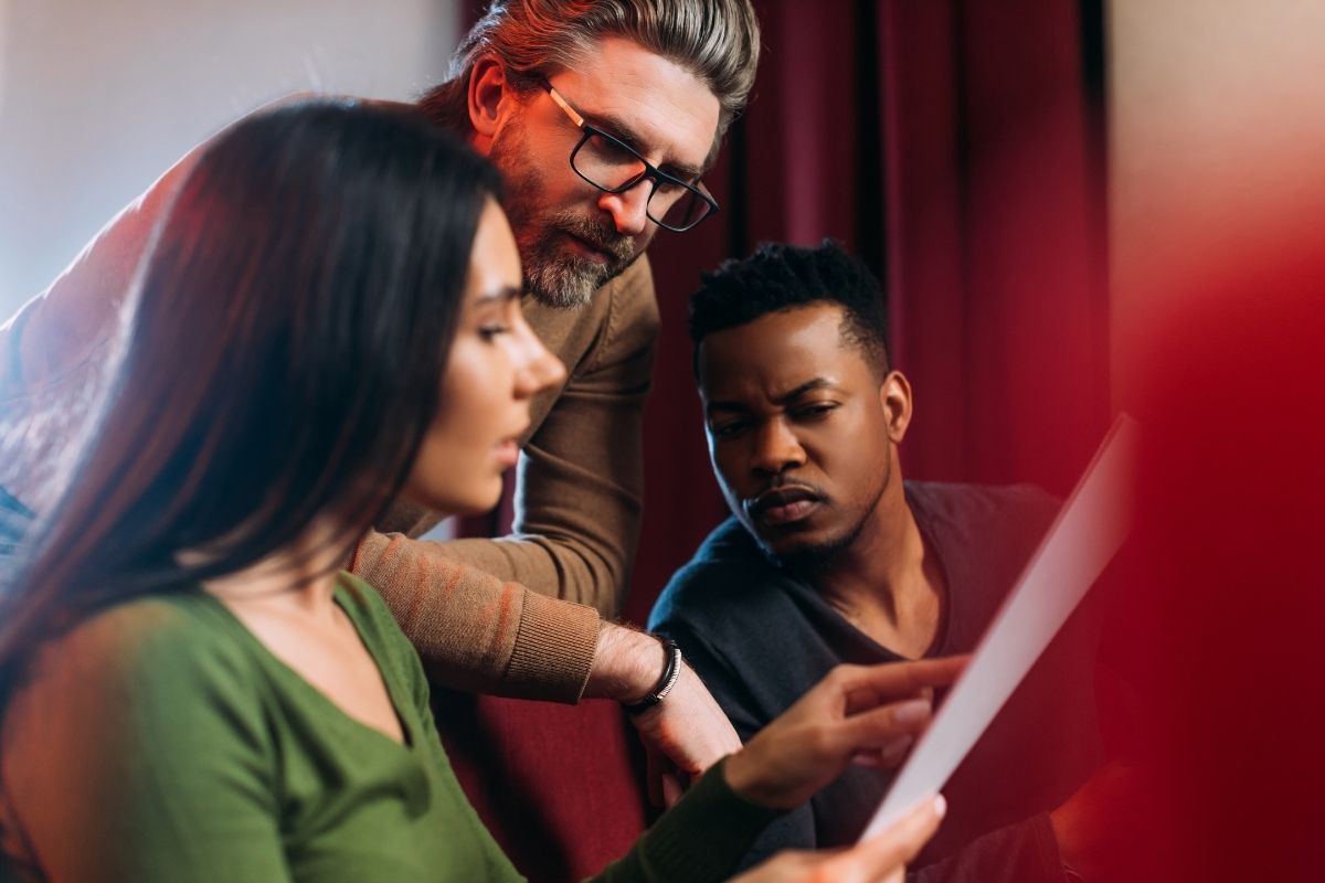 An actor and an actress reading script with the director.