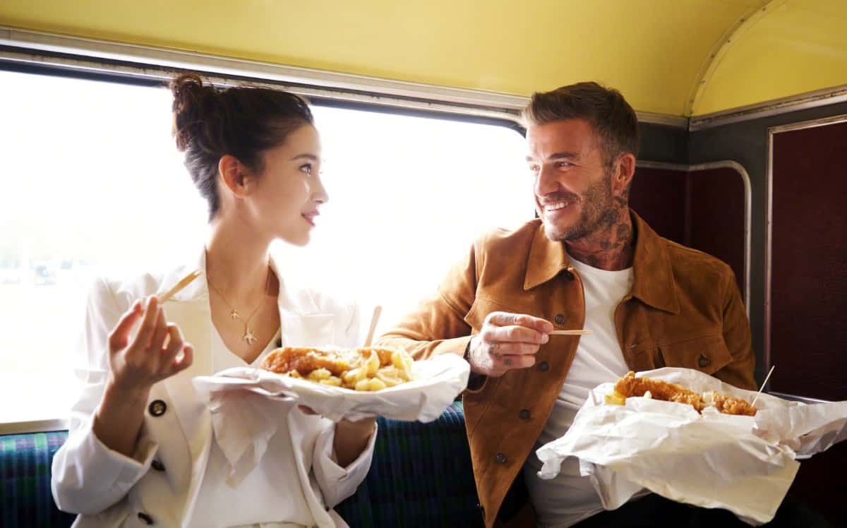 Angela Baby and David Beckham eating fried fish and chips on a movie set outdoors.