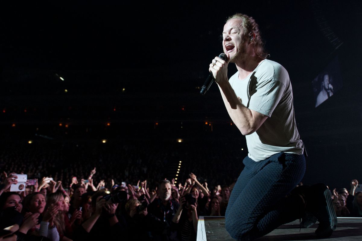 A man singing out load in a concert kneeling.