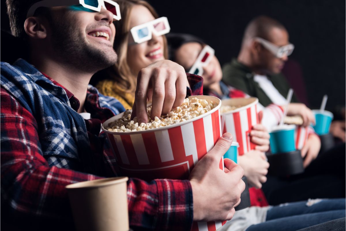 A group of friends in a 3d glasses watching in cinema eating popcorn.