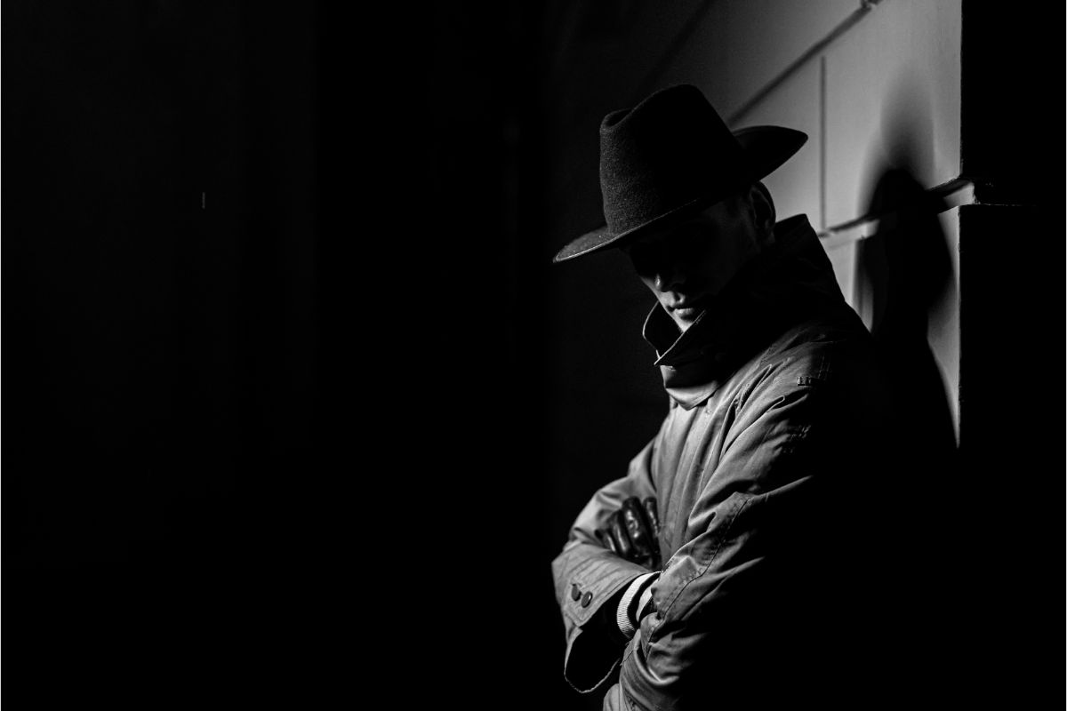 A dark silhouette of a man in a raincoat with a hat at night.