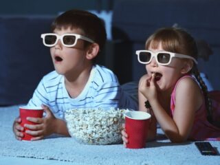 Siblings watching movie in their home while wearing 3D glasses.