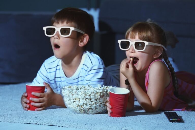 Siblings watching movie in their home while wearing 3D glasses.